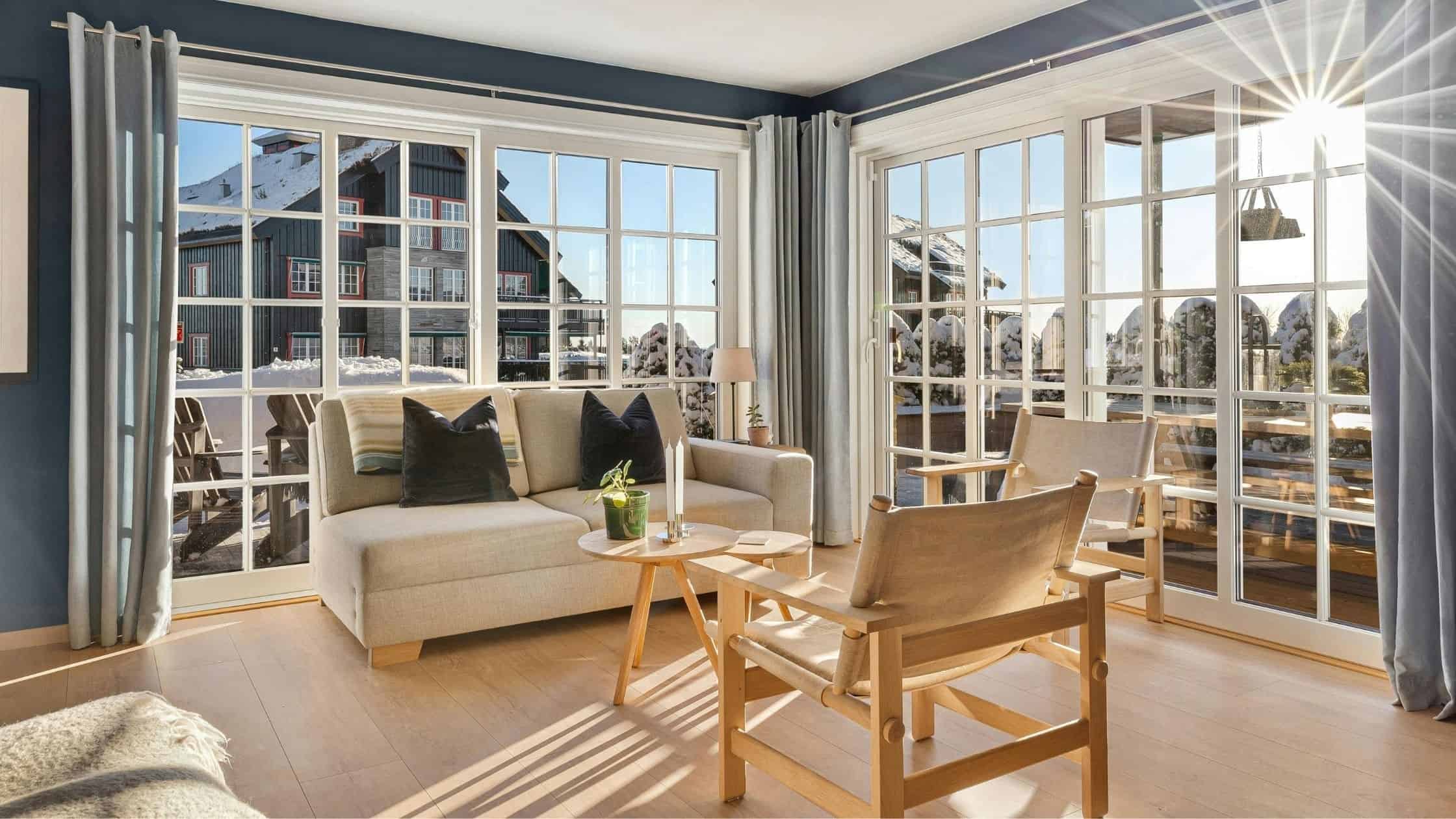 Sunlit living room with large windows, cozy sofa, and wooden chairs, showcasing quality window views.