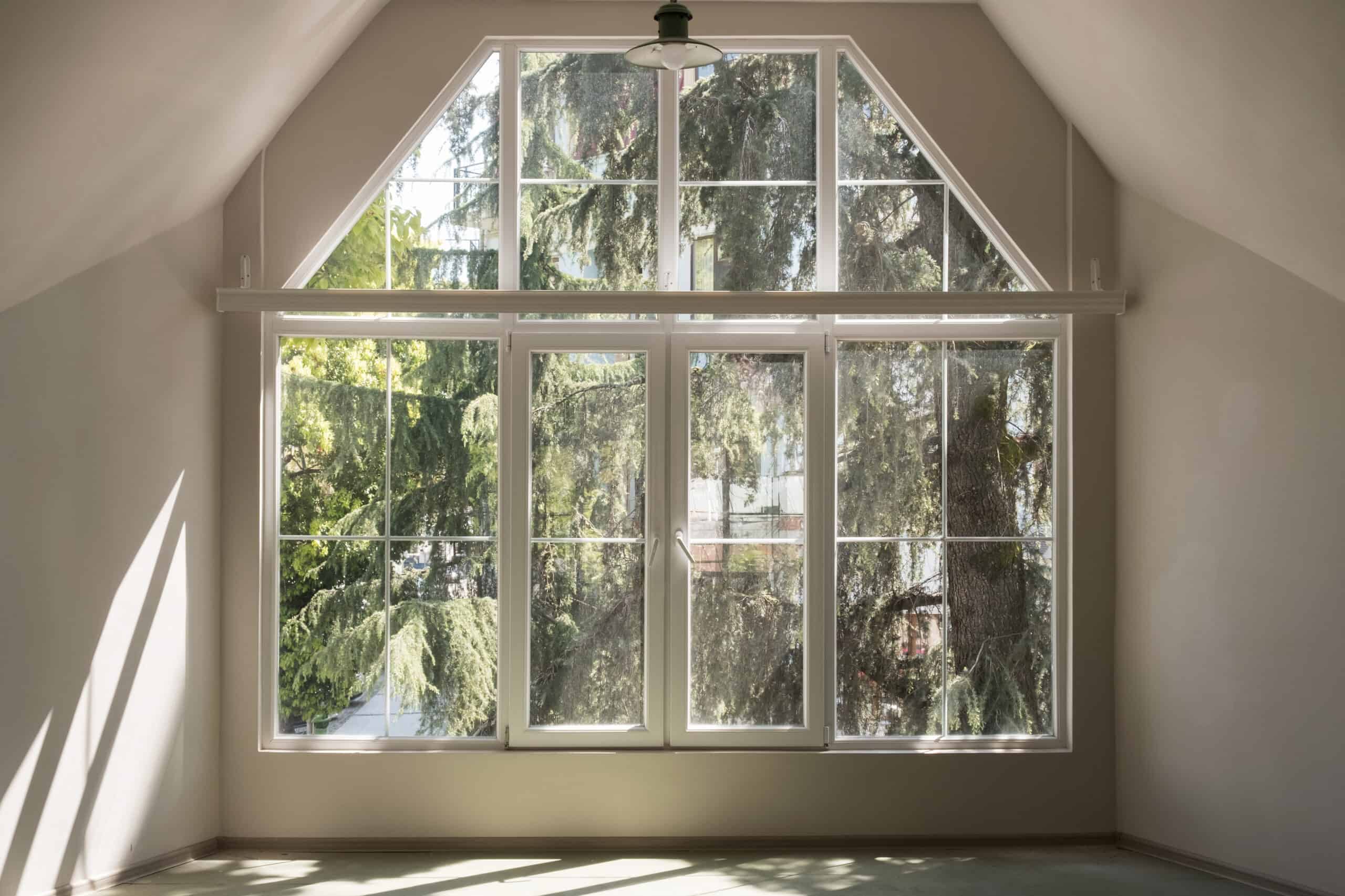 Bright large window with multiple panes in an attic room, overlooking trees outside.